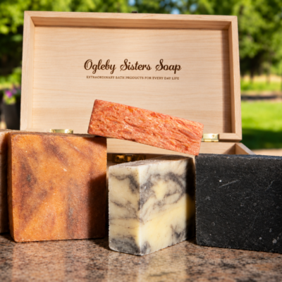 5 bars of handmade soap sitting in front of wooden box branded with name ogleby sisters soap with spring background